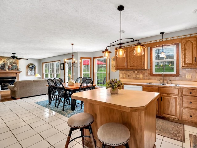 kitchen with a kitchen island, white dishwasher, a sink, light countertops, and light tile patterned flooring