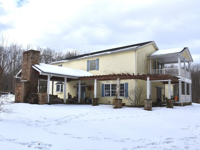 snow covered property featuring a balcony, a chimney, and a porch