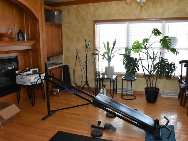 workout area featuring light wood-type flooring, visible vents, and a glass covered fireplace