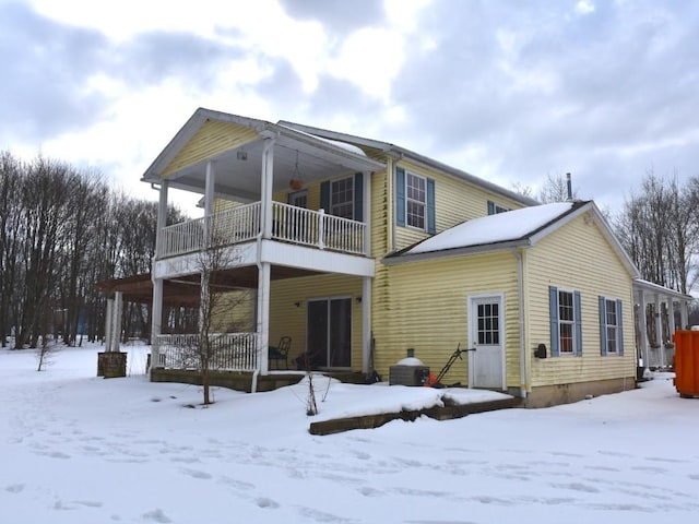 snow covered rear of property with a balcony and covered porch