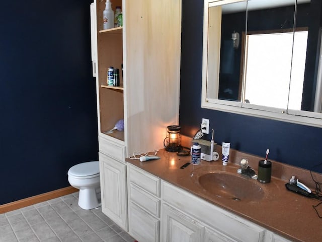 bathroom with double vanity, toilet, a sink, baseboards, and tile patterned floors