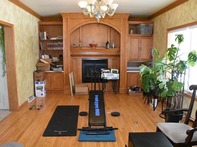 workout area with a notable chandelier, a glass covered fireplace, light wood-style flooring, and crown molding