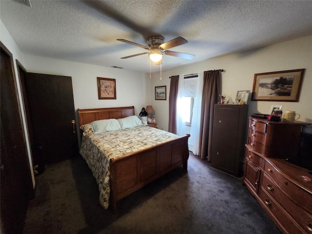 bedroom featuring a textured ceiling, dark carpet, visible vents, and a ceiling fan