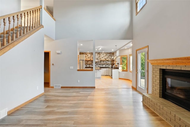 living room featuring light wood-type flooring, a fireplace, and a high ceiling