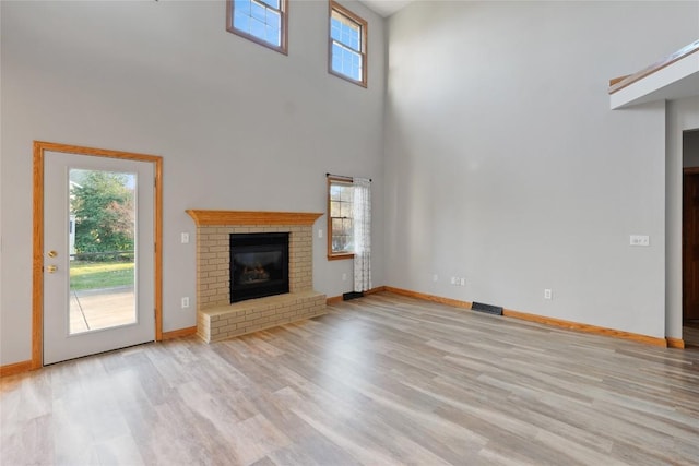 unfurnished living room with light hardwood / wood-style floors, a fireplace, and a high ceiling