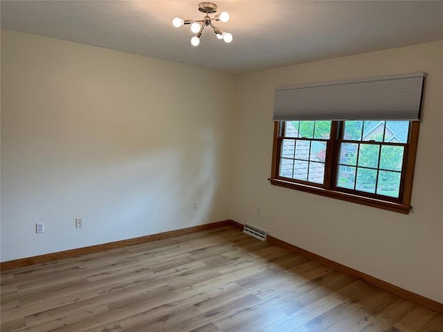 spare room with light hardwood / wood-style floors and an inviting chandelier