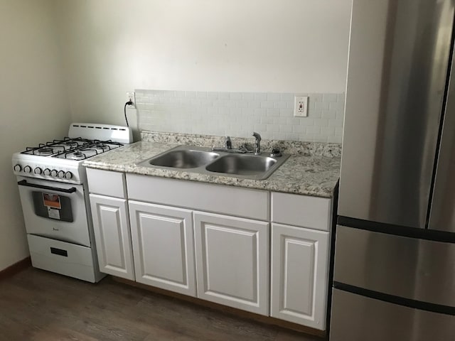 kitchen featuring stainless steel fridge, white gas range oven, tasteful backsplash, sink, and white cabinetry