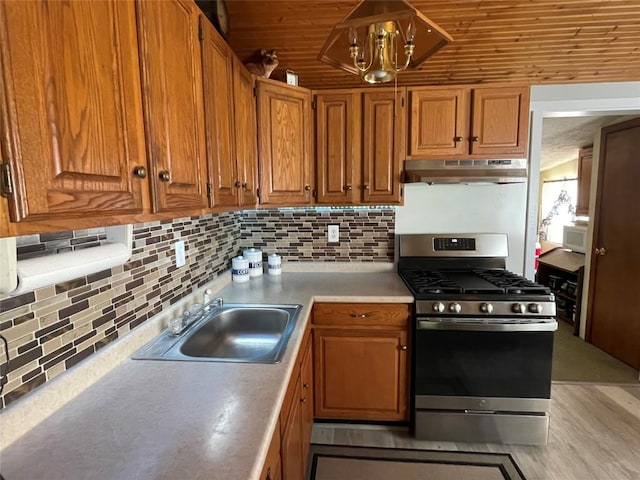 11694 Oakfield Rd, Conneaut Lake, PA 16316 - kitchen with stainless steel gas stove, under cabinet range hood, light countertops, brown cabinets, and tasteful backsplash