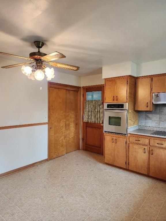 kitchen featuring brown cabinets, tasteful backsplash, light countertops, oven, and exhaust hood