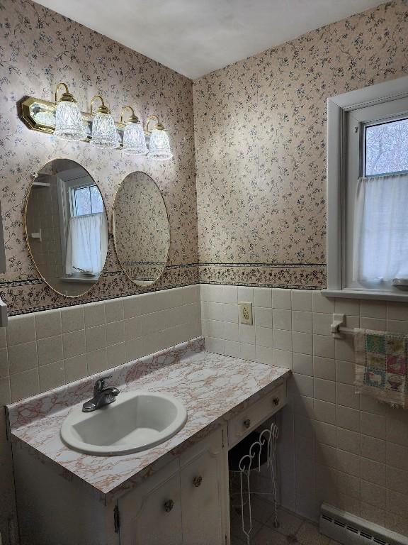 bathroom featuring wallpapered walls, wainscoting, vanity, a baseboard heating unit, and tile walls