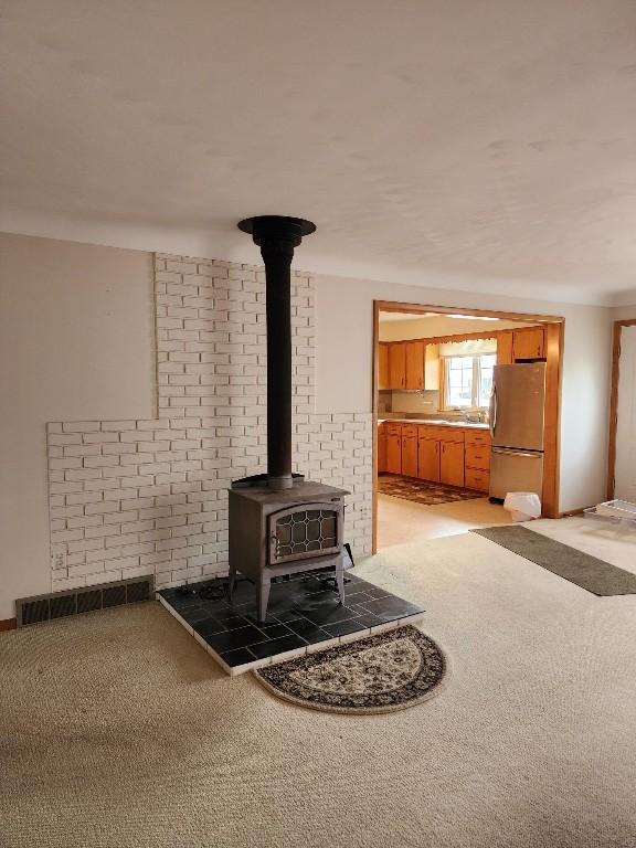 room details with a wood stove, visible vents, carpet flooring, and freestanding refrigerator