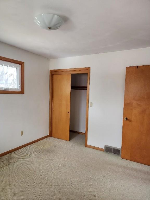 unfurnished bedroom featuring baseboards, a closet, visible vents, and light colored carpet