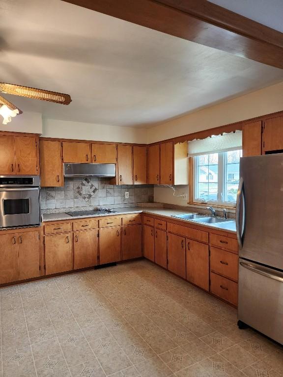 kitchen featuring decorative backsplash, brown cabinets, stainless steel appliances, under cabinet range hood, and a sink