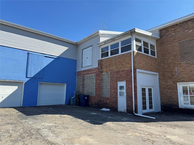 rear view of property featuring a garage, french doors, and brick siding