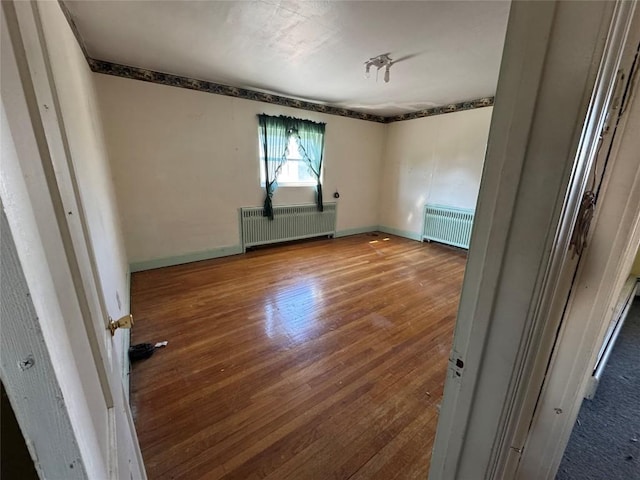 unfurnished room with baseboards, radiator heating unit, wood finished floors, and radiator