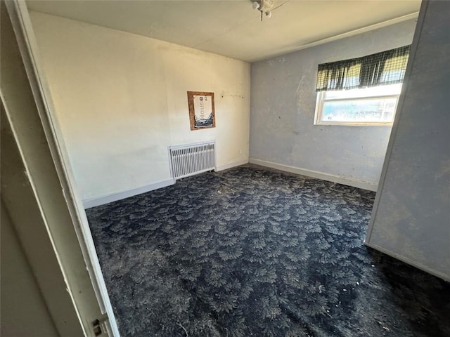 carpeted empty room featuring baseboards and radiator