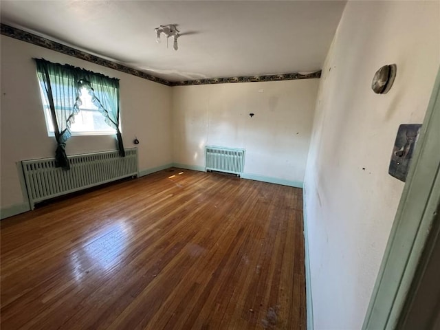 empty room with radiator, baseboards, wood-type flooring, and radiator heating unit