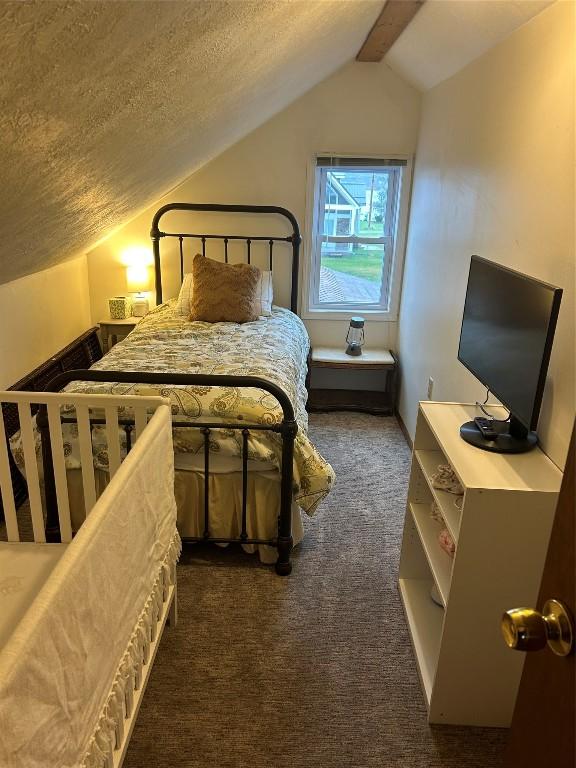 bedroom with vaulted ceiling, a textured ceiling, and dark colored carpet