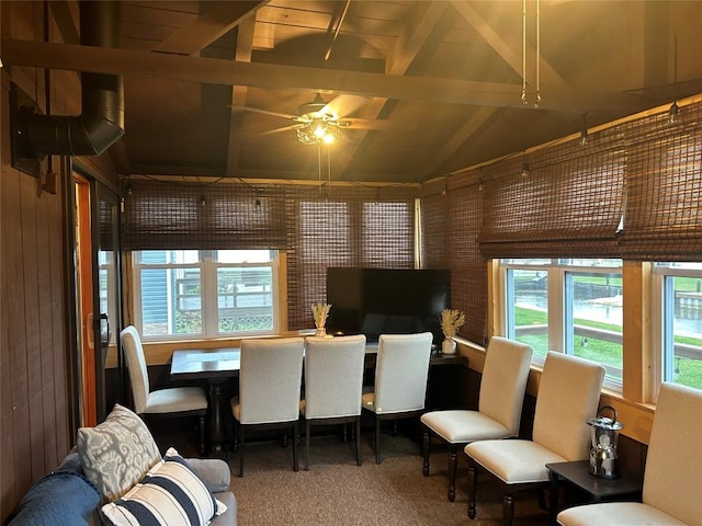 carpeted dining room featuring ceiling fan, plenty of natural light, lofted ceiling with beams, and wood walls