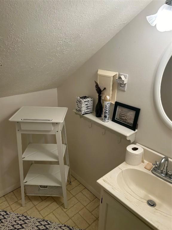 bathroom with vanity, a textured ceiling, vaulted ceiling, and tile patterned flooring