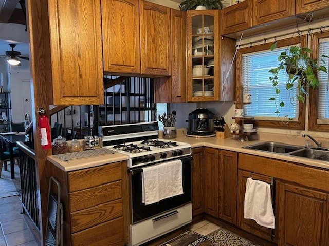 kitchen with white gas stove, light tile patterned flooring, sink, and ceiling fan