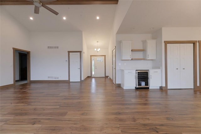 unfurnished living room featuring ceiling fan with notable chandelier, dark hardwood / wood-style flooring, a towering ceiling, and beverage cooler