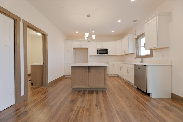 kitchen featuring appliances with stainless steel finishes, pendant lighting, hardwood / wood-style floors, a center island, and white cabinetry