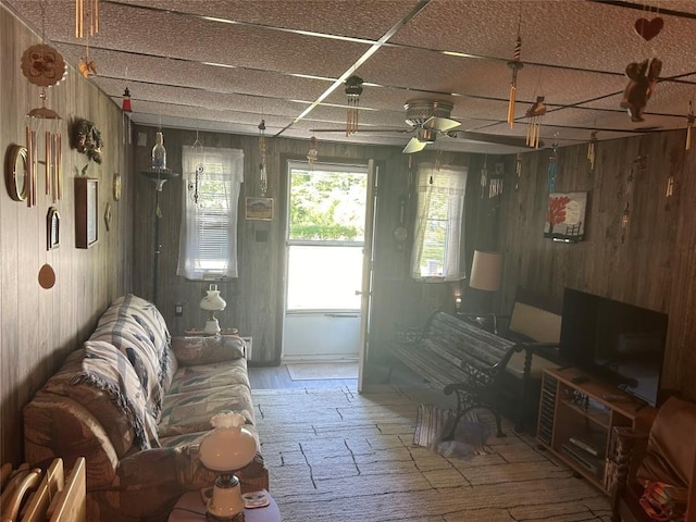 interior space featuring ceiling fan, a drop ceiling, and wooden walls