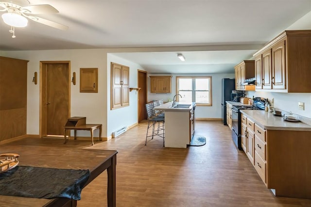 kitchen with electric range, sink, a baseboard radiator, a breakfast bar area, and hardwood / wood-style flooring