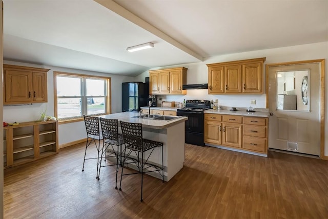 kitchen with a breakfast bar, a kitchen island with sink, black appliances, dark hardwood / wood-style floors, and lofted ceiling