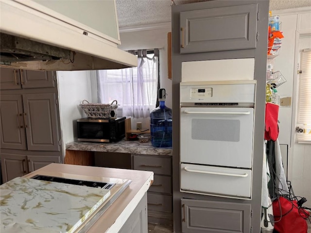 kitchen with a warming drawer, light countertops, ornamental molding, a textured ceiling, and under cabinet range hood