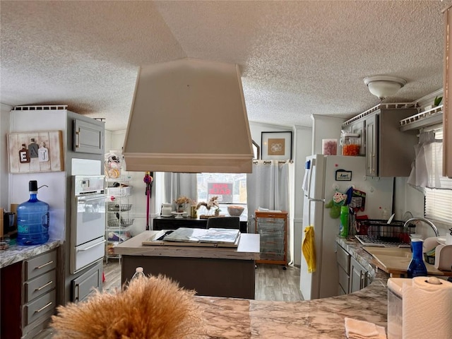 kitchen with light wood-style flooring, oven, a textured ceiling, gray cabinetry, and a warming drawer