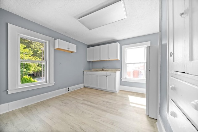 kitchen with white cabinetry, sink, light hardwood / wood-style floors, and white refrigerator