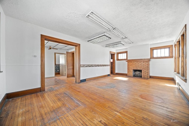 unfurnished living room featuring light hardwood / wood-style floors, a textured ceiling, and a brick fireplace