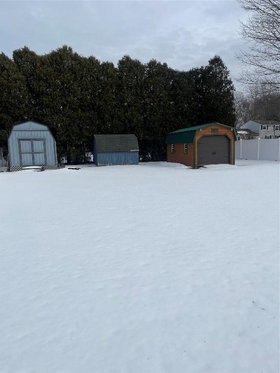 yard covered in snow featuring a garage, an outdoor structure, and a shed