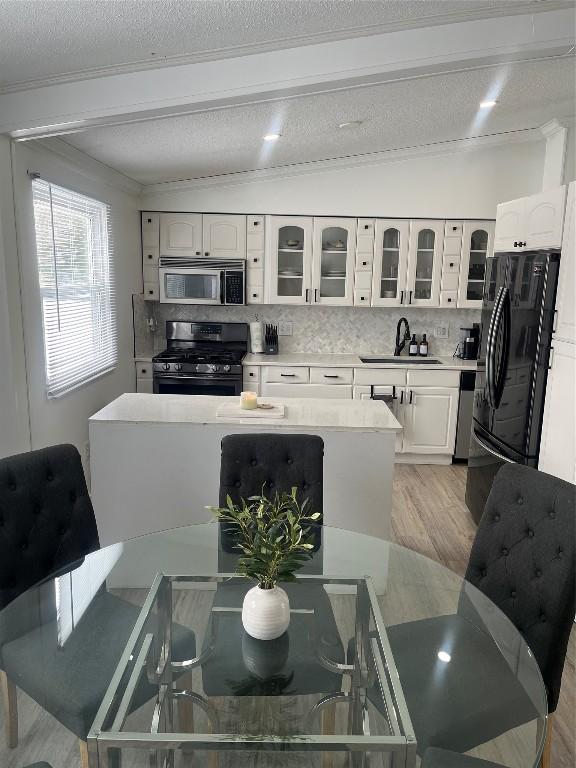 kitchen with glass insert cabinets, light countertops, black appliances, white cabinetry, and a sink