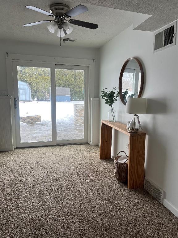 doorway to outside with a textured ceiling, carpet flooring, and visible vents