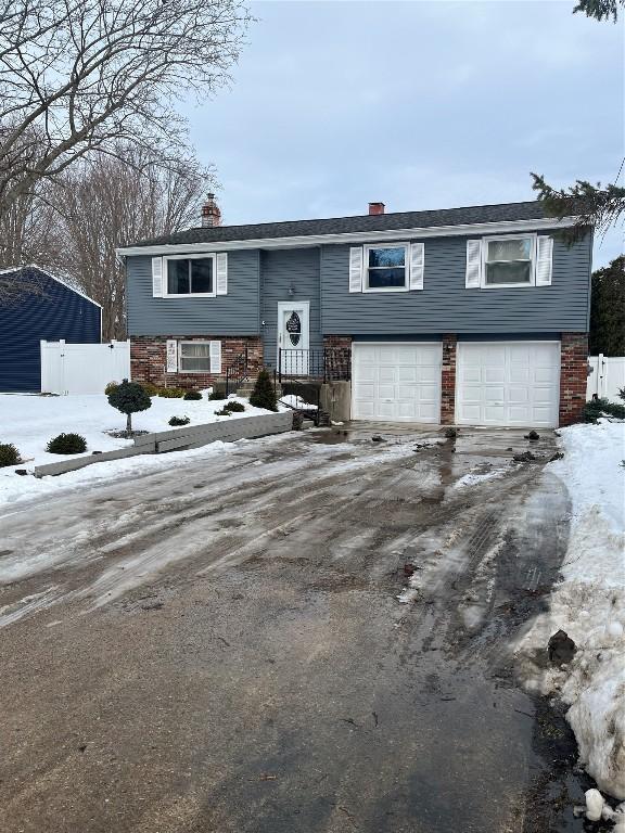 bi-level home with a garage, driveway, and fence