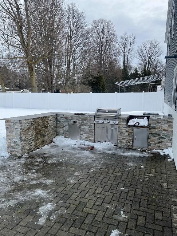 snow covered patio featuring a grill, a fenced backyard, and area for grilling