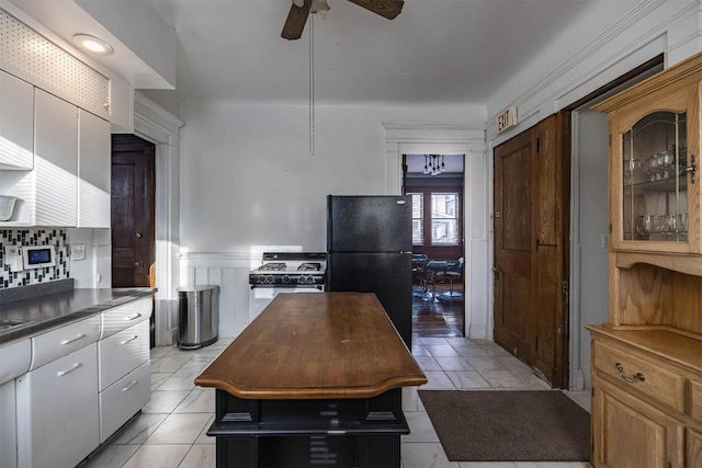 kitchen with light tile patterned flooring, black fridge, white range with gas stovetop, and white cabinets