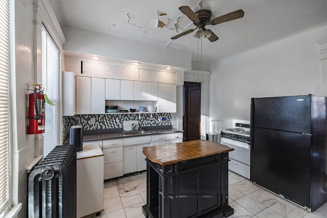 kitchen featuring white cabinetry, sink, decorative backsplash, white gas range oven, and black fridge