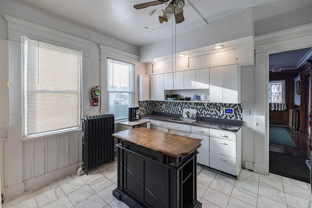 kitchen with sink, ceiling fan, backsplash, radiator heating unit, and white cabinets