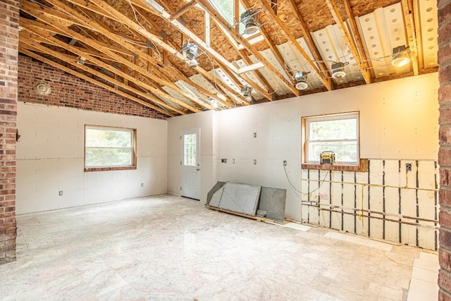 interior space featuring lofted ceiling, a healthy amount of sunlight, and brick wall