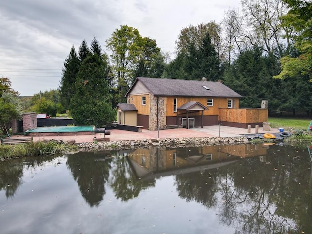 back of property with a water view, a patio, and a covered pool