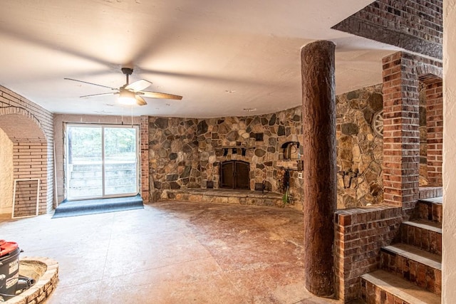 unfurnished living room featuring ceiling fan, a fireplace, and brick wall