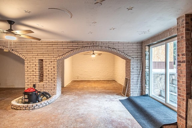 unfurnished living room featuring ceiling fan and brick wall