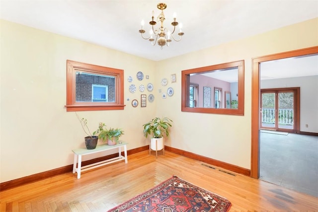 hall with wood finished floors, baseboards, and a notable chandelier