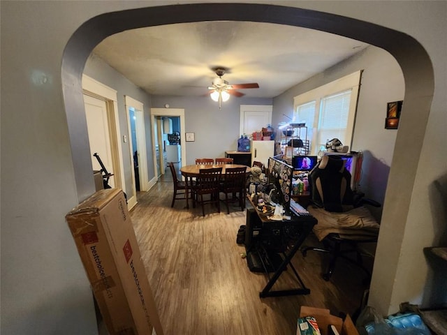 dining area with arched walkways, a ceiling fan, and light wood-type flooring