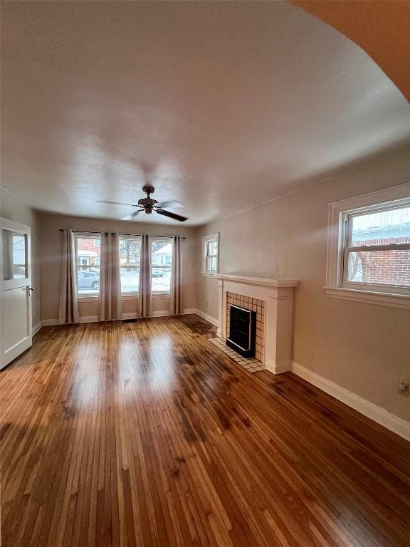 unfurnished living room featuring a healthy amount of sunlight, a fireplace, wood-type flooring, and ceiling fan