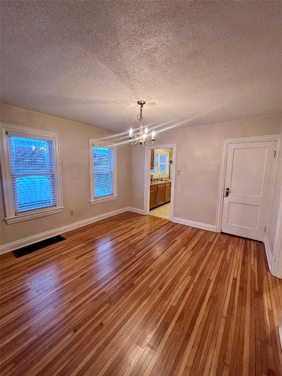 spare room with a chandelier, light hardwood / wood-style flooring, and a textured ceiling